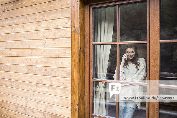 Young woman standing at the window using smartphone