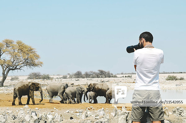 Namibia  Etosha Nationalpark  Fotograf fotografiert Elefanten in der Nähe eines Wasserlochs.