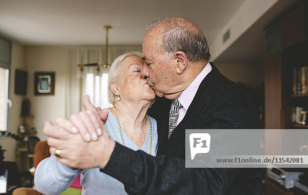 Senior couple kissing and dancing at home