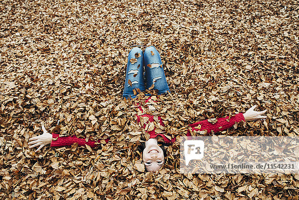 Frau mit ausgestreckten Armen auf Waldboden liegend mit Herbstblättern bedeckt