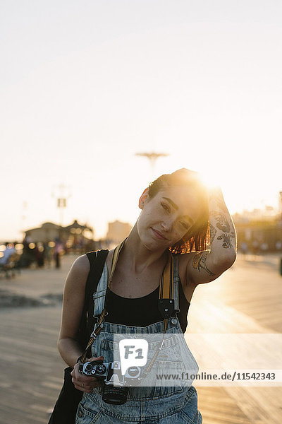 USA,  New York,  Coney Island,  junge Frau mit Kamera bei Sonnenuntergang
