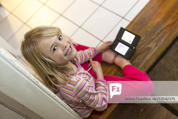 Portrait des lächelnden kleinen Mädchens beim Spielen mit der Handheld-Spielkonsole