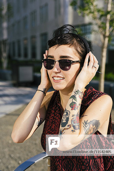 Portrait of tattooed young woman with headphones and sunglasses