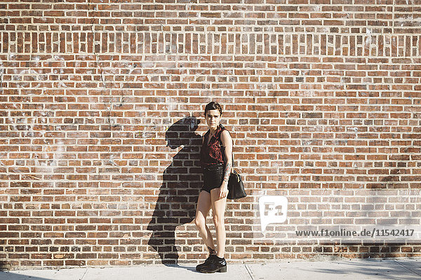 Portrait of young woman leaning against brick wall
