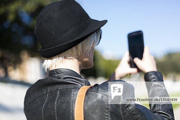 Rückansicht einer blonden Frau  die schwarz trägt und mit dem Smartphone ein Möbelstück nimmt