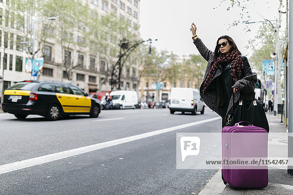 Spain  Barcelona  young woman with suitcase hailing a taxi