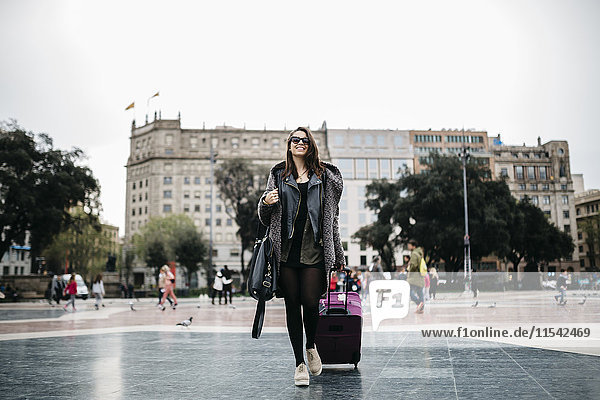 Spain  Barcelona  young woman with suitcase walking on Placa Catalunya