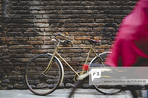 Oldtimer-Fahrrad,  das sich an eine Ziegelwand lehnt,  während der Radfahrer vorbeifährt.