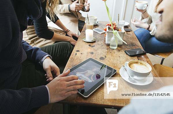 Man in a cafe showing picture on digital tablet to friends