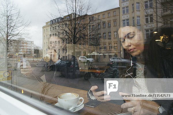Frau in einem Café hinter der Fensterscheibe mit digitalem Tablett