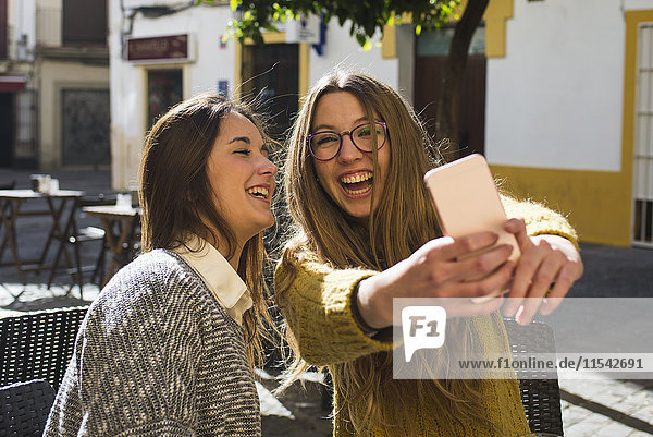 Lachende junge Frau nimmt einen Selfie mit ihrem Freund im Straßencafé.