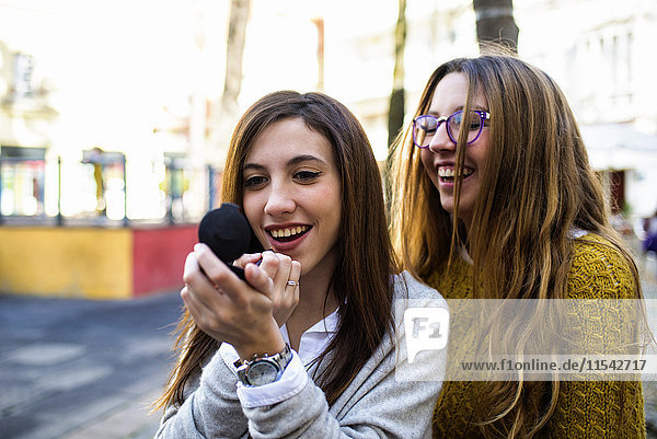 portrait of young woman applying lipstick while her friend watching