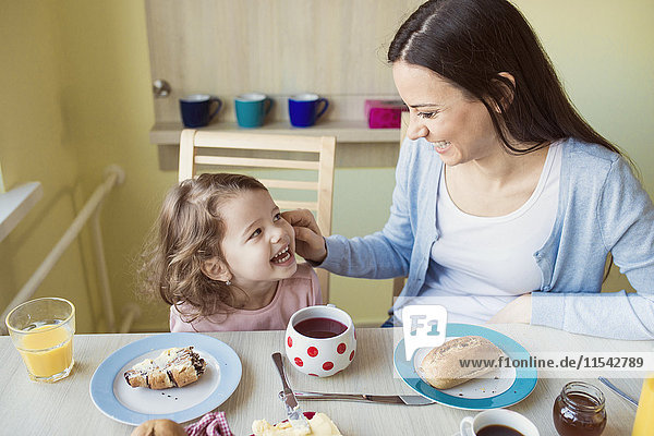 Porträt der Mutter und ihrer kleinen Tochter  die sich am Frühstückstisch amüsieren.