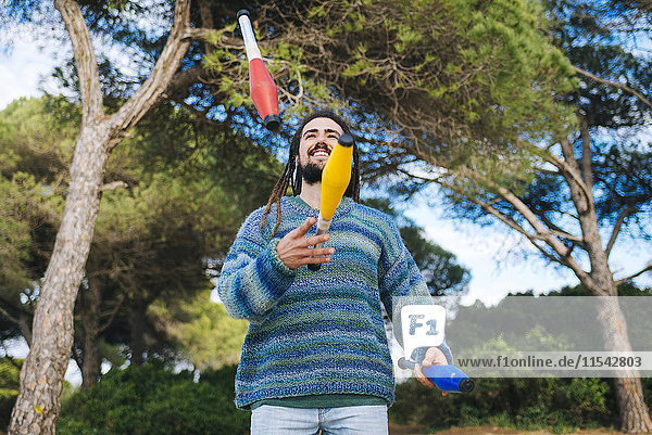 Junger Mann mit Dreadlocks jongliert mit Jonglierkeulen