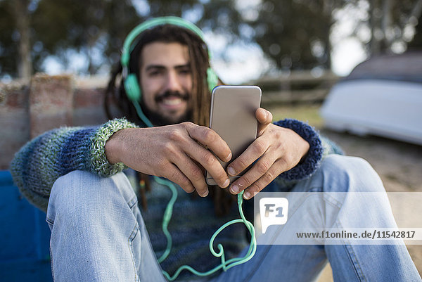 Junger Mann mit Dreadlocks  der Musik hört und das Smartphone benutzt.