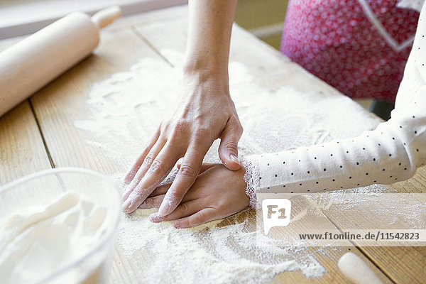 Die Hände der Frau und ihrer kleinen Tochter auf der mit Mehl bedeckten Tischplatte  Nahaufnahme