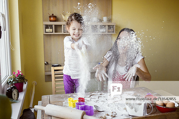 Mutter und ihre kleine Tochter werfen Mehl in die Luft in der Küche.