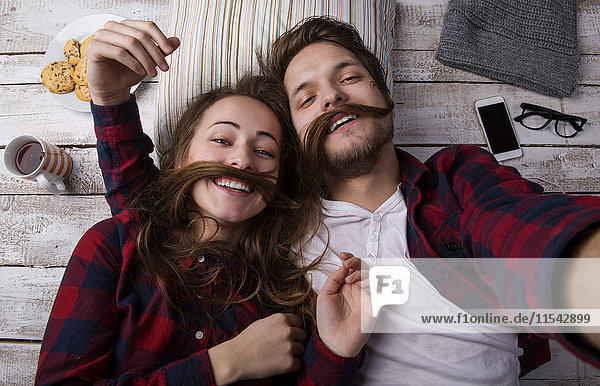 Portrait of young couple lying on the floor taking a selfie