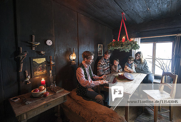 Familie hört einem Mann zu  der in einem Bauernhauszimmer im Advent Zither spielt.