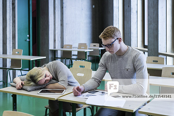 Zwei Schüler im Klassenzimmer mit einer Frau die auf dem Schreibtisch schläft.