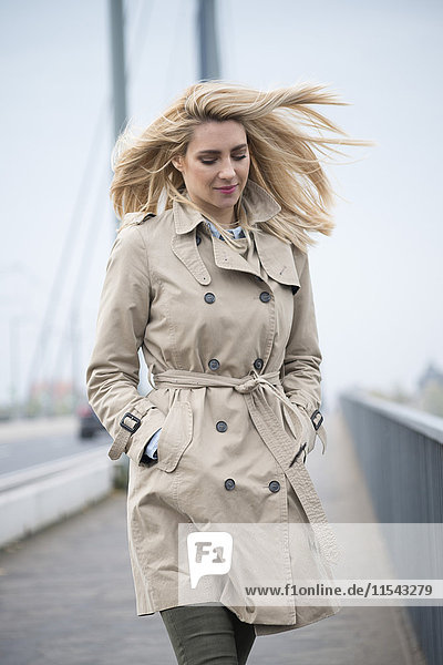 Portrait of young woman wearing trench coat walking on a bridge