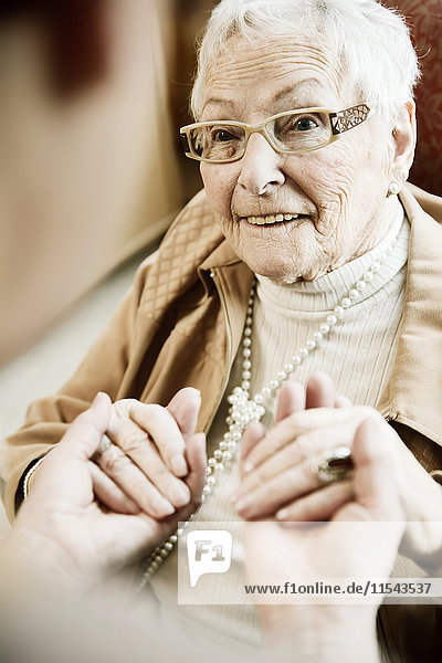 Porträt einer älteren Frau mit Alzheimer-Krankheit,  die die Hände ihrer erwachsenen Tochter hält.