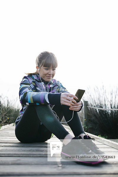 Junge Frau entspannt sich nach dem Laufen  mit dem Smartphone