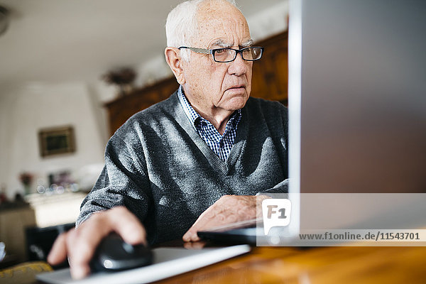 Porträt eines ernsthaft aussehenden älteren Mannes mit Laptop zu Hause