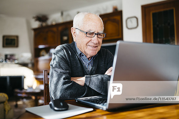 Porträt eines lächelnden älteren Mannes mit Laptop zu Hause