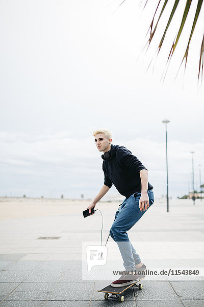 Spanien  Torredembarra  junger Mann mit Smartphone auf dem Skateboard