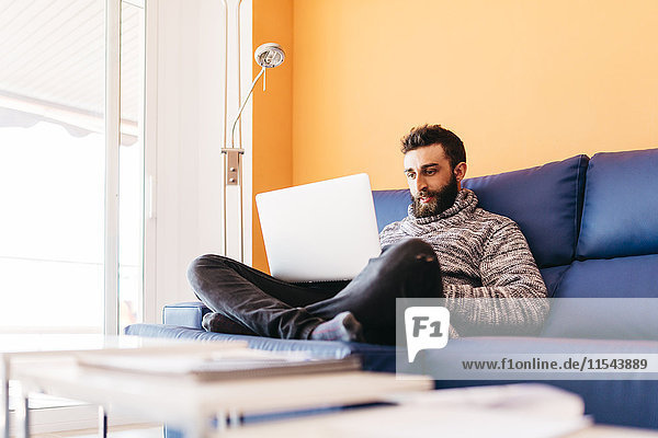 Bearded young man working at home relaxed sitting on the couch  using laptop