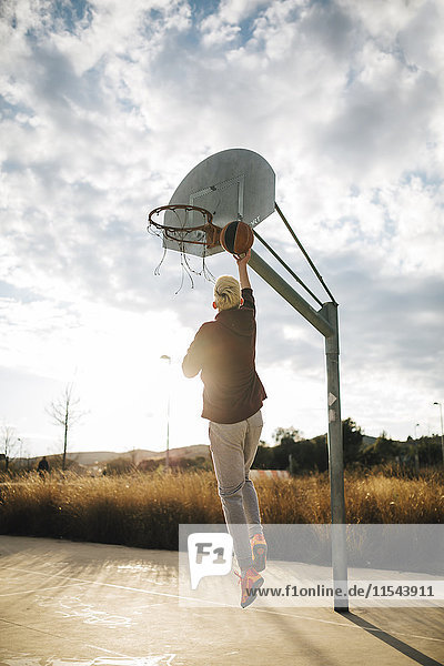 Junger Mann spielt Basketball auf einem Außenplatz