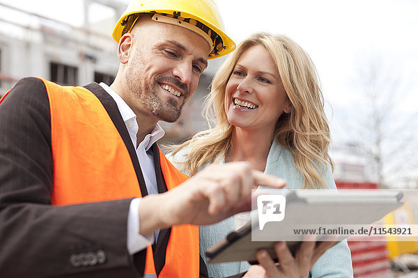Lächelnder Mann mit Schutzhelm im Gespräch mit Frau auf der Baustelle