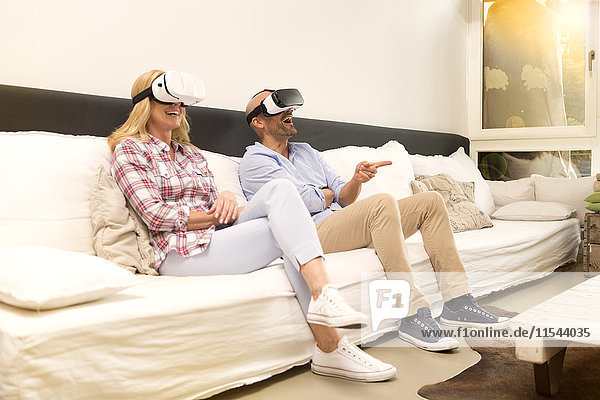 Couple sitting on couch at home using Virtual Reality Glasses