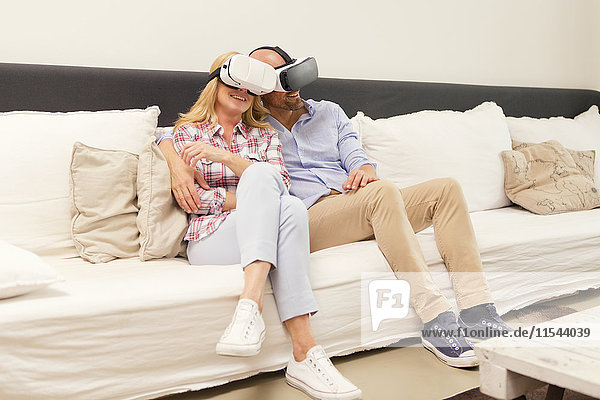Paar sitzend Kopf an Kopf auf der Couch zu Hause mit Virtual Reality Brille