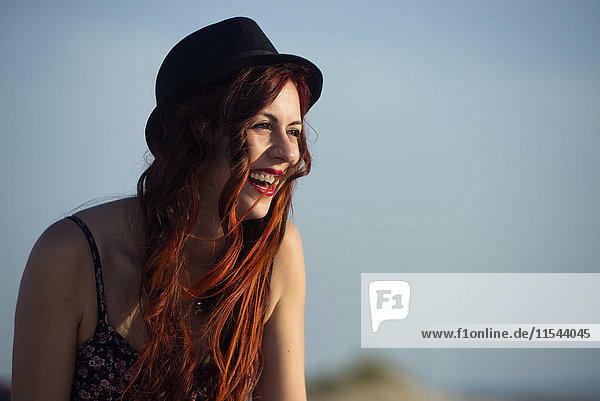Portrait of laughing woman wearing hat in front of blue sky