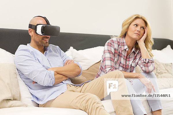Mann mit Virtual Reality Brille sitzt auf der Couch neben seiner gelangweilten Frau