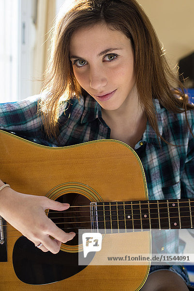 Porträt einer lächelnden jungen Frau beim Gitarrespielen