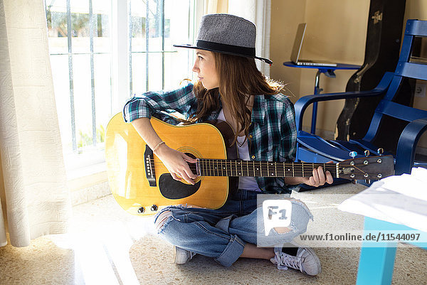 Junge Frau sitzt auf dem Boden und spielt Gitarre.