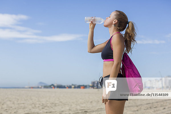 Brasilien  Rio de Janeiro  Copacabana  sportliche Frau mit Trinkwasser am Strand