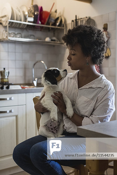 Junge Frau sitzend in der Küche mit ihrem Hund auf dem Schoß