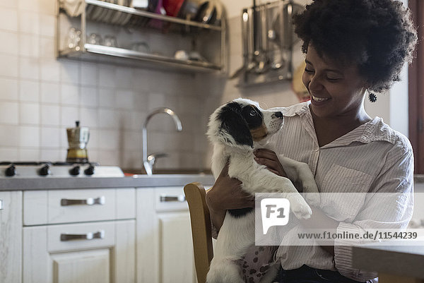 Happy young woman sitting in the kitchen with her dog on lap