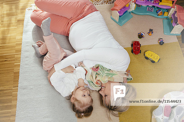 Schwangere Mutter und kleine Tochter beim Kuscheln auf dem Teppich zu Hause