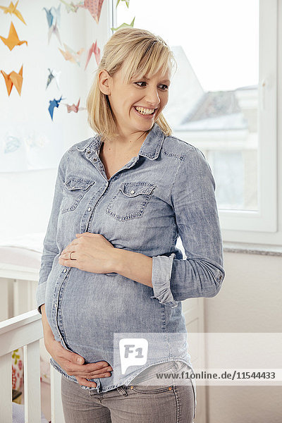 Porträt einer schwangeren Frau  die ihren Bauch im Kinderzimmer hält.