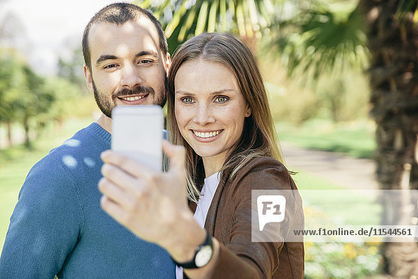 Glückliches Paar nimmt Selfie mit Smartphone in einem botanischen Garten