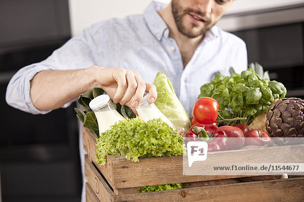 Junger Mann mit Holzkiste mit frischem Gemüse und zwei Milchflaschen