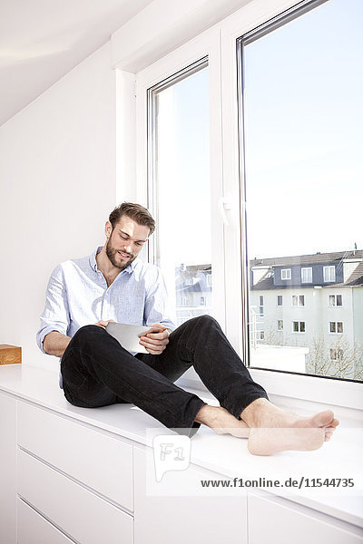 Junger Mann sitzt zu Hause auf dem Sideboard mit Mini-Tablett