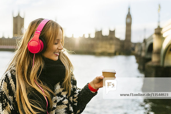 UK  London  junge Frau hört Musik und trinkt Kaffee in der Nähe der Westminster Bridge