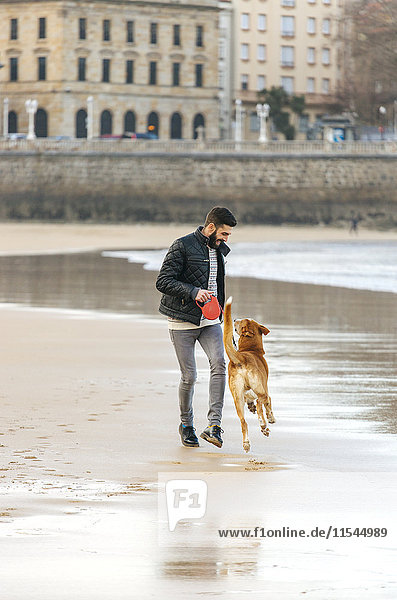 Spanien  Gijon  Mann spielt am Strand mit seinem Hund