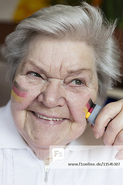 Porträt einer selbstbewussten Seniorin  die deutsche Nationalfarben auf die Wange malt.